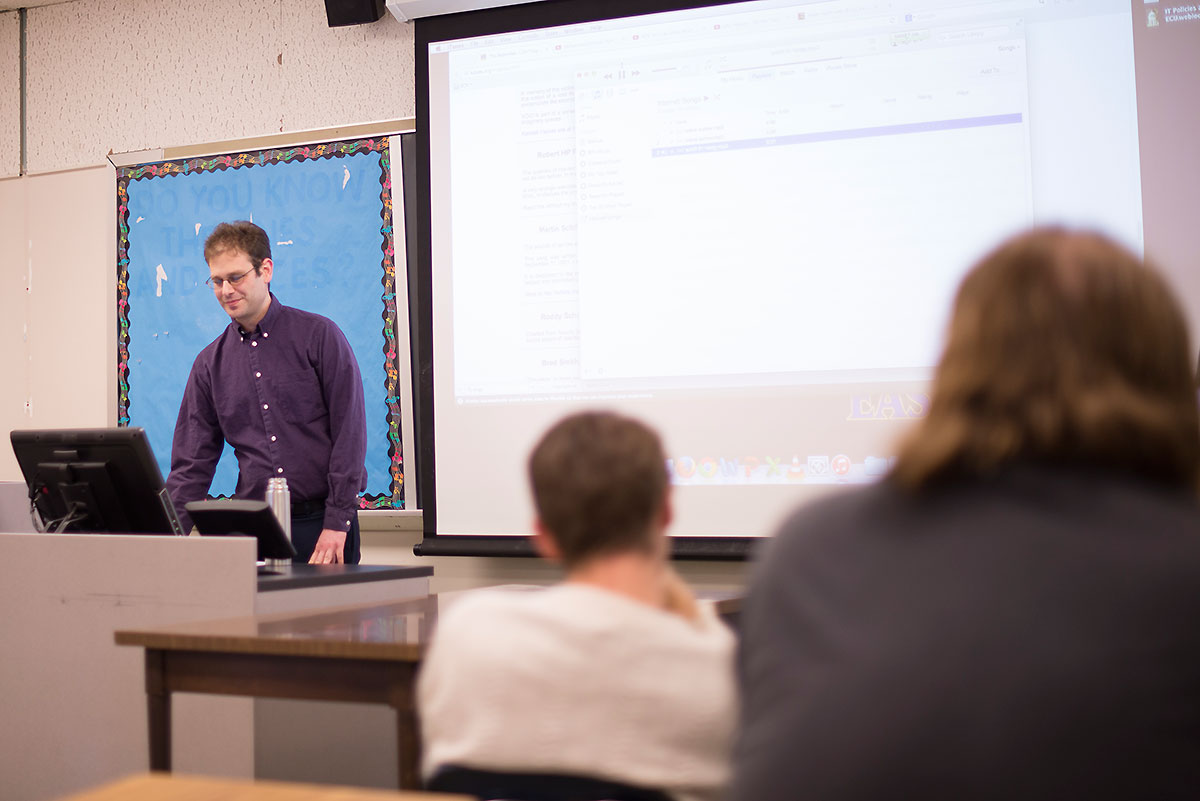 Dr. Guberman stands at a podium next to a screen in front of students.